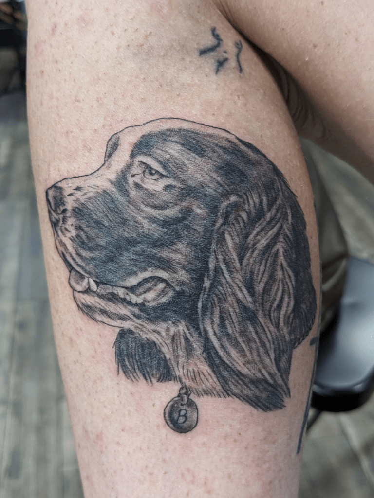 Realism tattoo of a portrait of a pet dog. Black and grey tattoo showing fur texture.