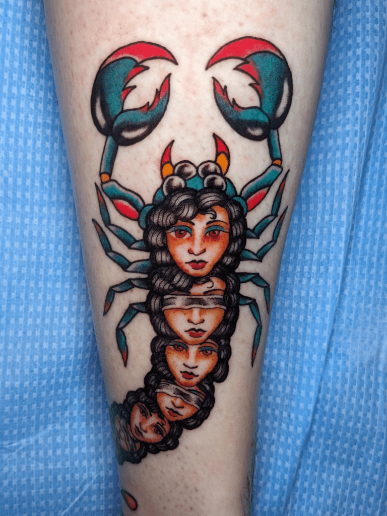 An American Traditional tattoo of a scorpion made up of lady heads. Turquoise and red are the prominent colors throughout the scorpion.